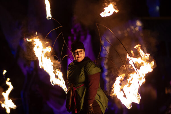 A woman with large metal bat wings on her back with the tips of the wings lit on fire.