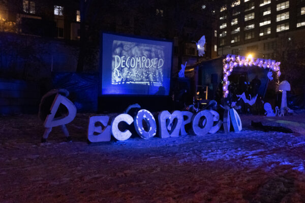 The outdoor stage of a show, with 2 foot tall paper mache letters on the ground, spelling out Decomposed, and a large screen in the background with the word decomposed on it.