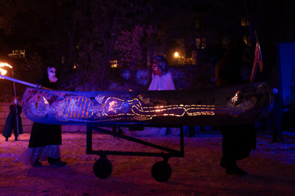 Puppeteers carrying a metal canoe (lit up from the inside) with a skeleton cut out of the side.