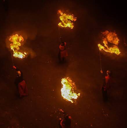 View from above of four fire performers carrying poles with large flames on top.