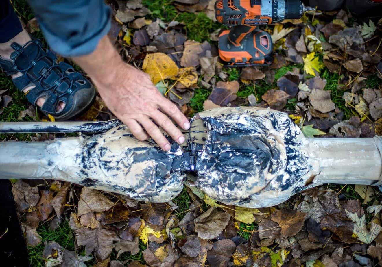 A tight shot of the femur and tibia of a 16 foot tall skeleton puppet laying on the ground of a park covered in autumn foliage. A hand is touching the joint.