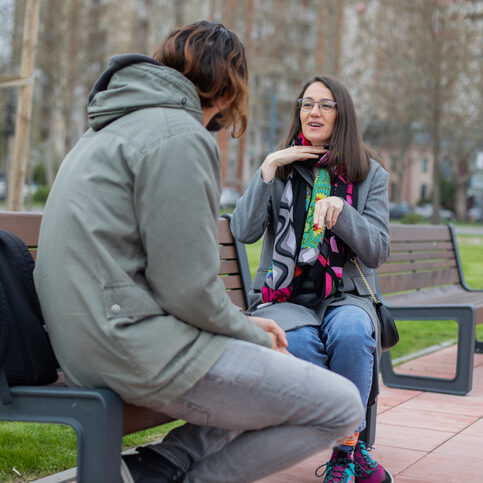 Two young deaf people are hanging out in the public park. They are sitting on the park bench and speaking in sign language.