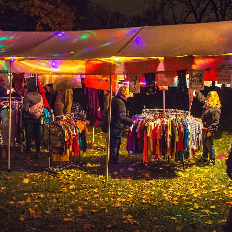 People shopping at a merchandise tent with colorful lights strunge around the tent.