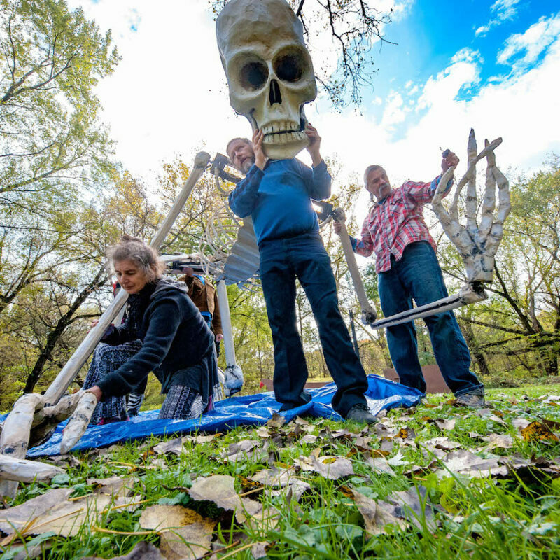 Three people working with a 12 foot skeleton puppet in a park.