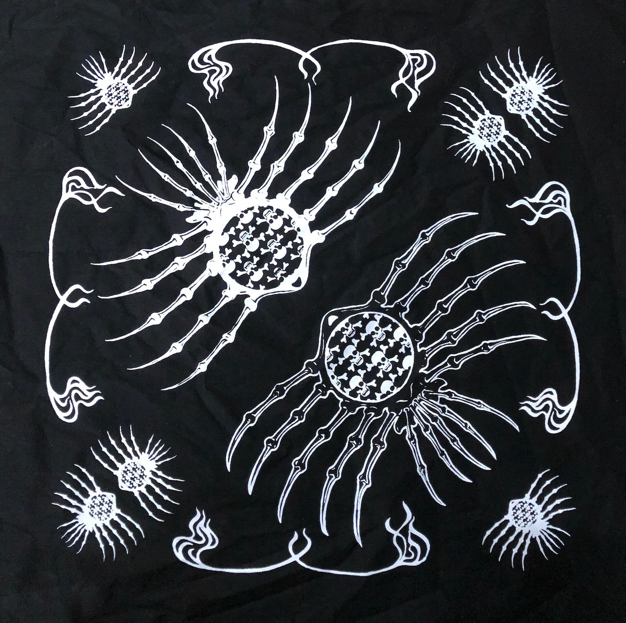 A screen print on black fabric of skulls inside spider or insect like outlines.